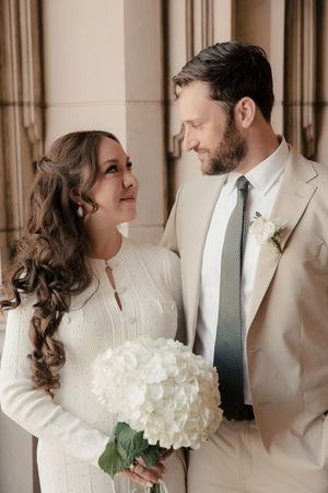 Couple in white attire shares intimate moments while holding a bouquet of white hydrangeas.