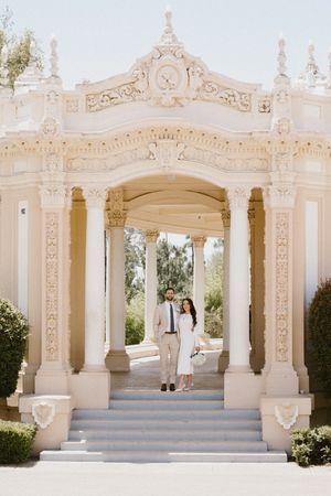 Ornate white classical pavilion with decorative columns and blue steps in a garden setting.