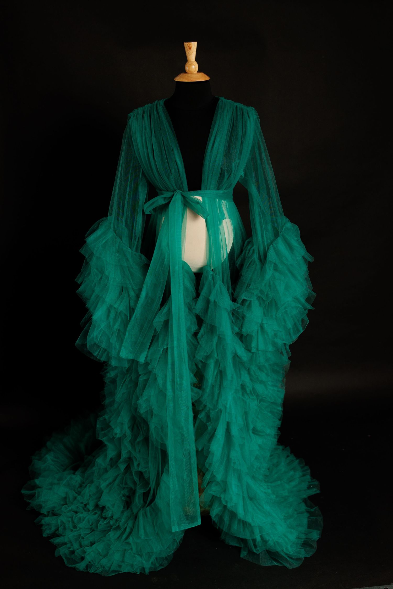 Emerald green sheer tulle robe with dramatic ruffled sleeves displayed on a black mannequin against dark background.