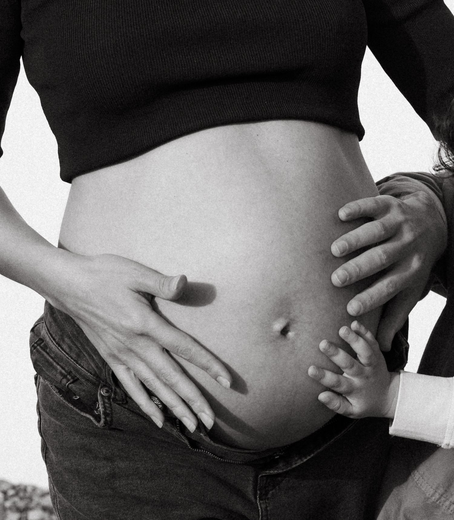 Black and white close-up of hands tenderly cradling a pregnant belly.