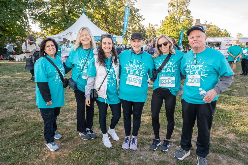Group of people wearing matching teal colored shirts gather outdoors for a community event.
