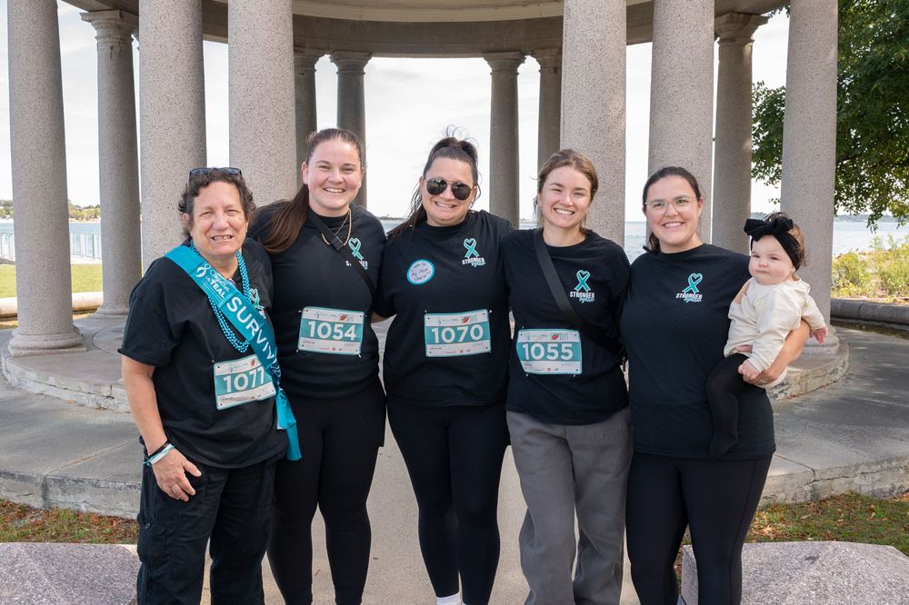 Group wearing matching black shirts poses together under outdoor columned structure at a community event.