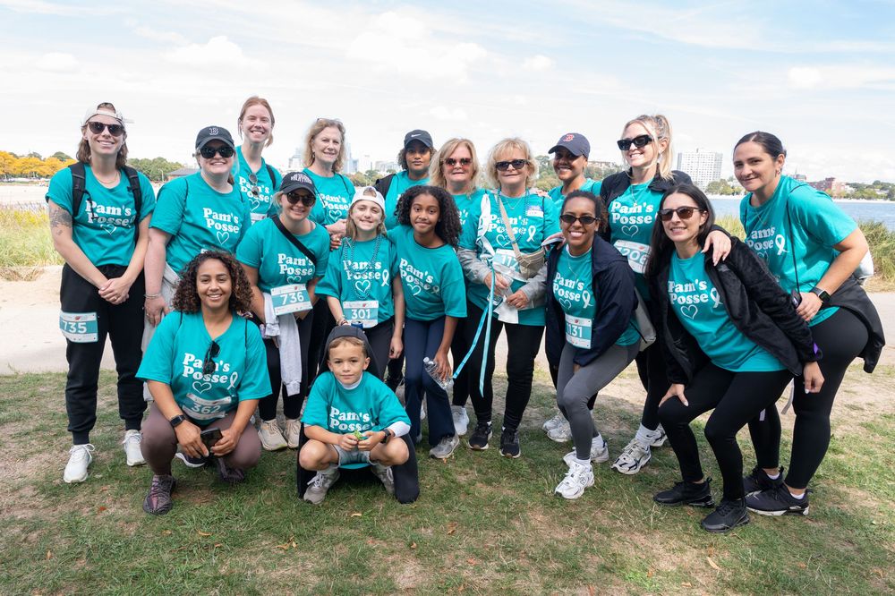 Group of volunteers wearing matching teal t-shirts pose together outdoors during community event.