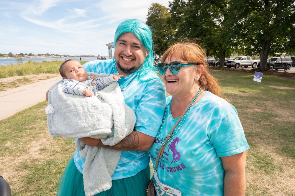 Three people in tie-dye shirts enjoying a sunny day at a lakeside park.
