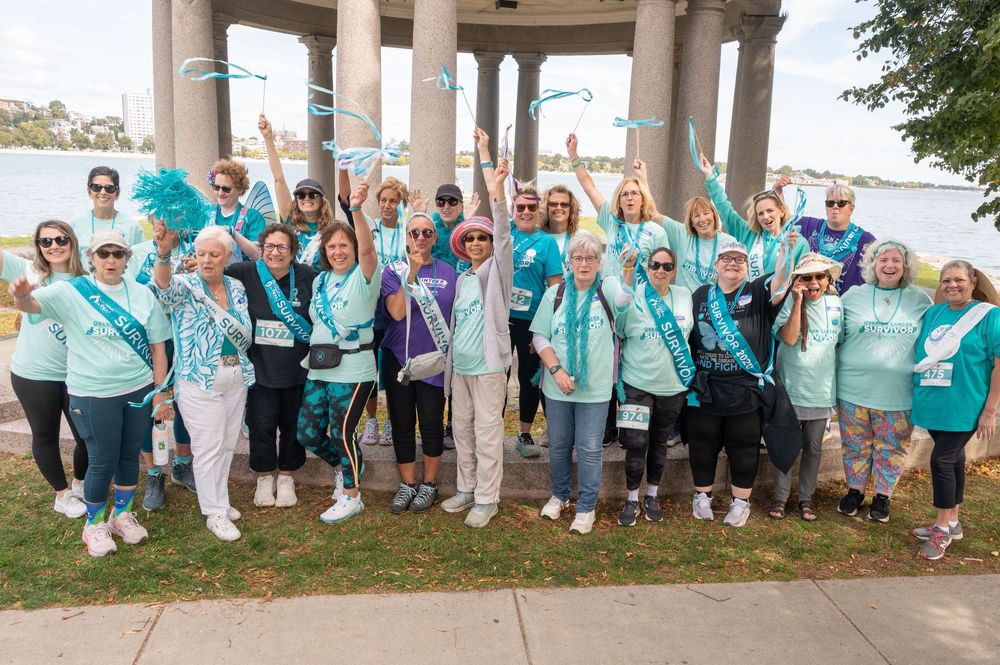 Large group in matching turquoise shirts gathered under gazebo for charity event photo.