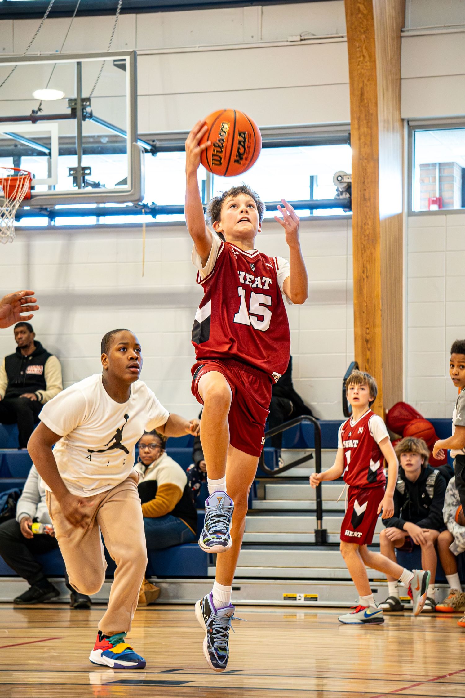 Youth basketball player in red jersey drives to the hoop during an indoor game.