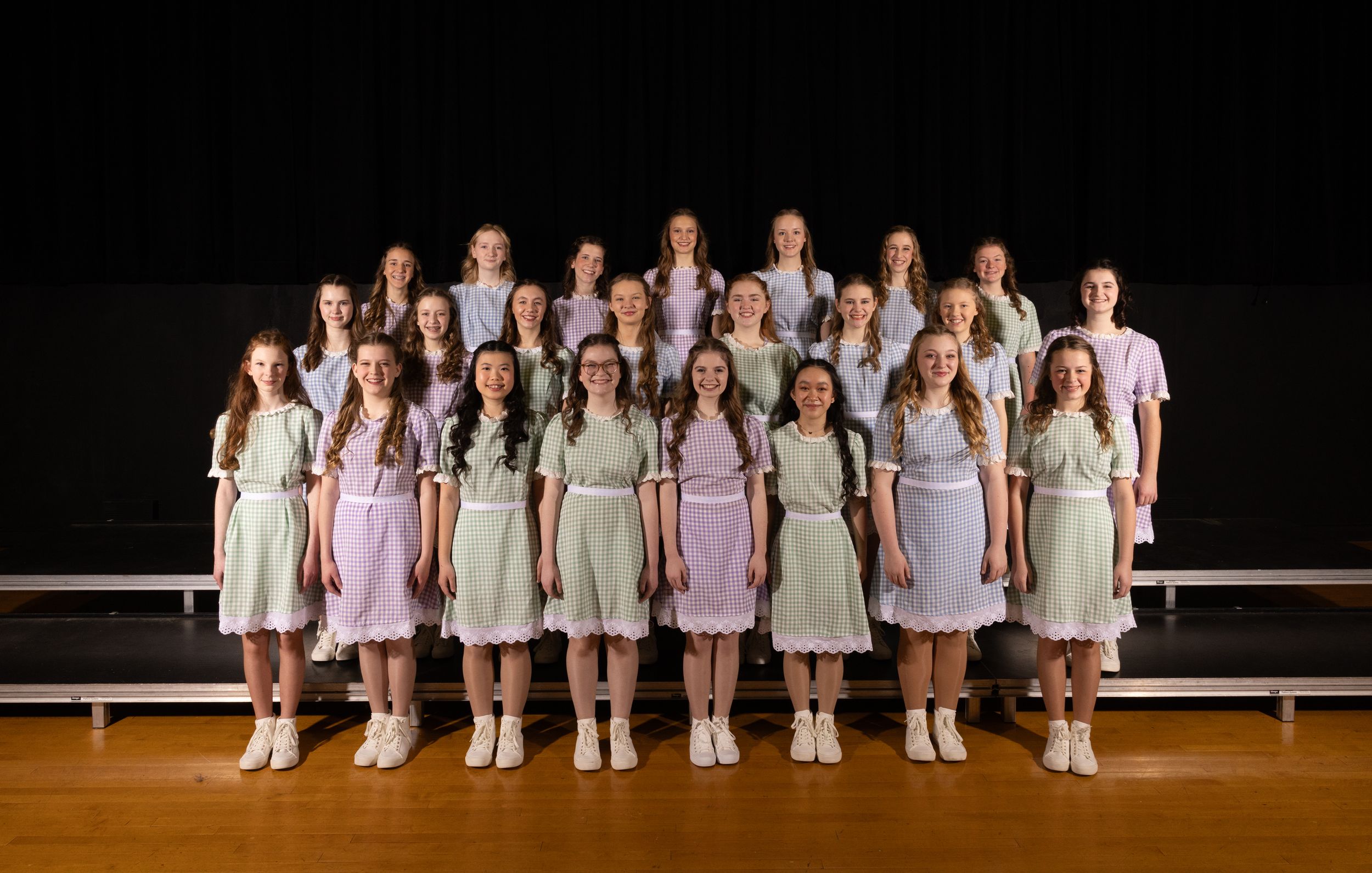 Dance ensemble in pale colored dresses poses together on performance stage.