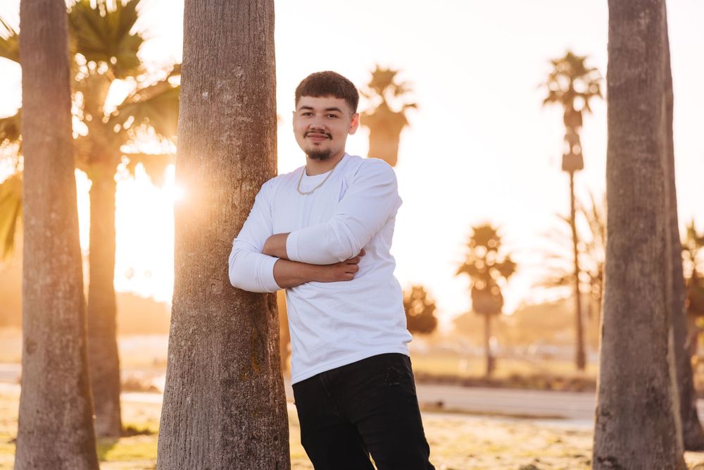 Relaxed outdoor portrait with palm trees silhouetted against sunset sky.
