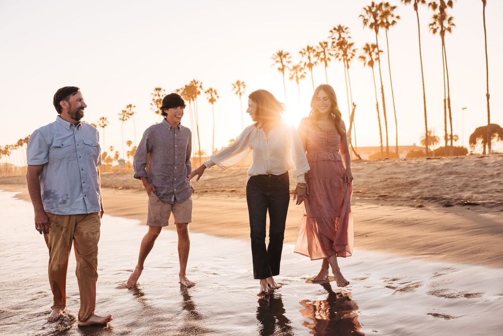 Couple strolling hand in hand on sandy beach with setting sun creating warm glow.