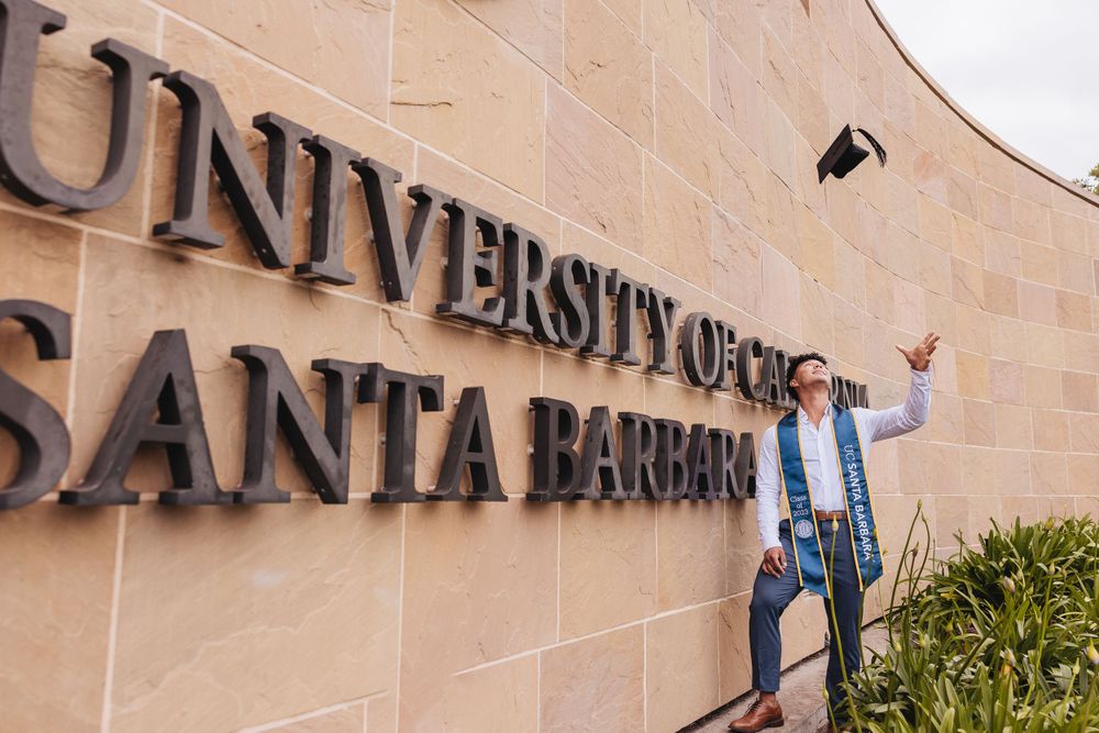 college senior throwing graduation hat in front of UCSB sign while taking pictures taken