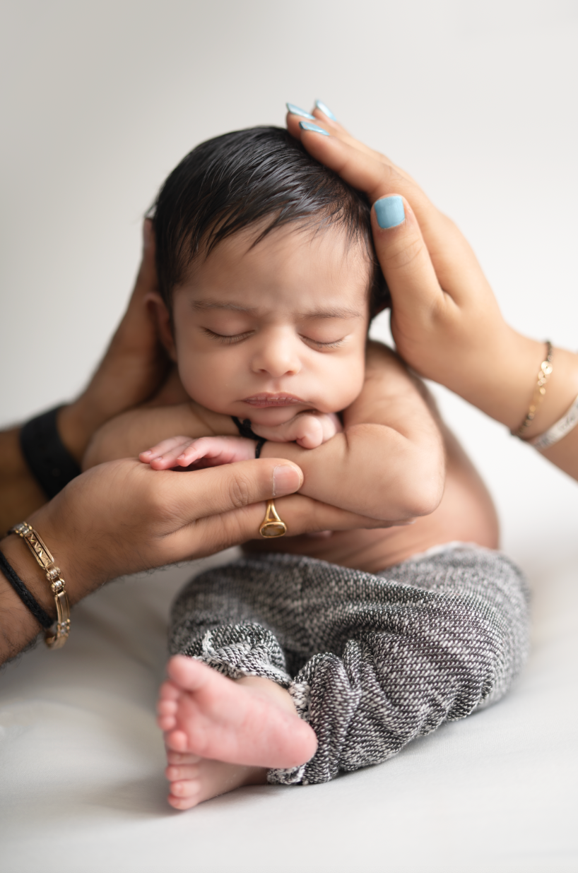 Peaceful sleeping newborn baby cradled in mother's hands, wearing gray knit pants, on white background. Embracing Life’s Beauty