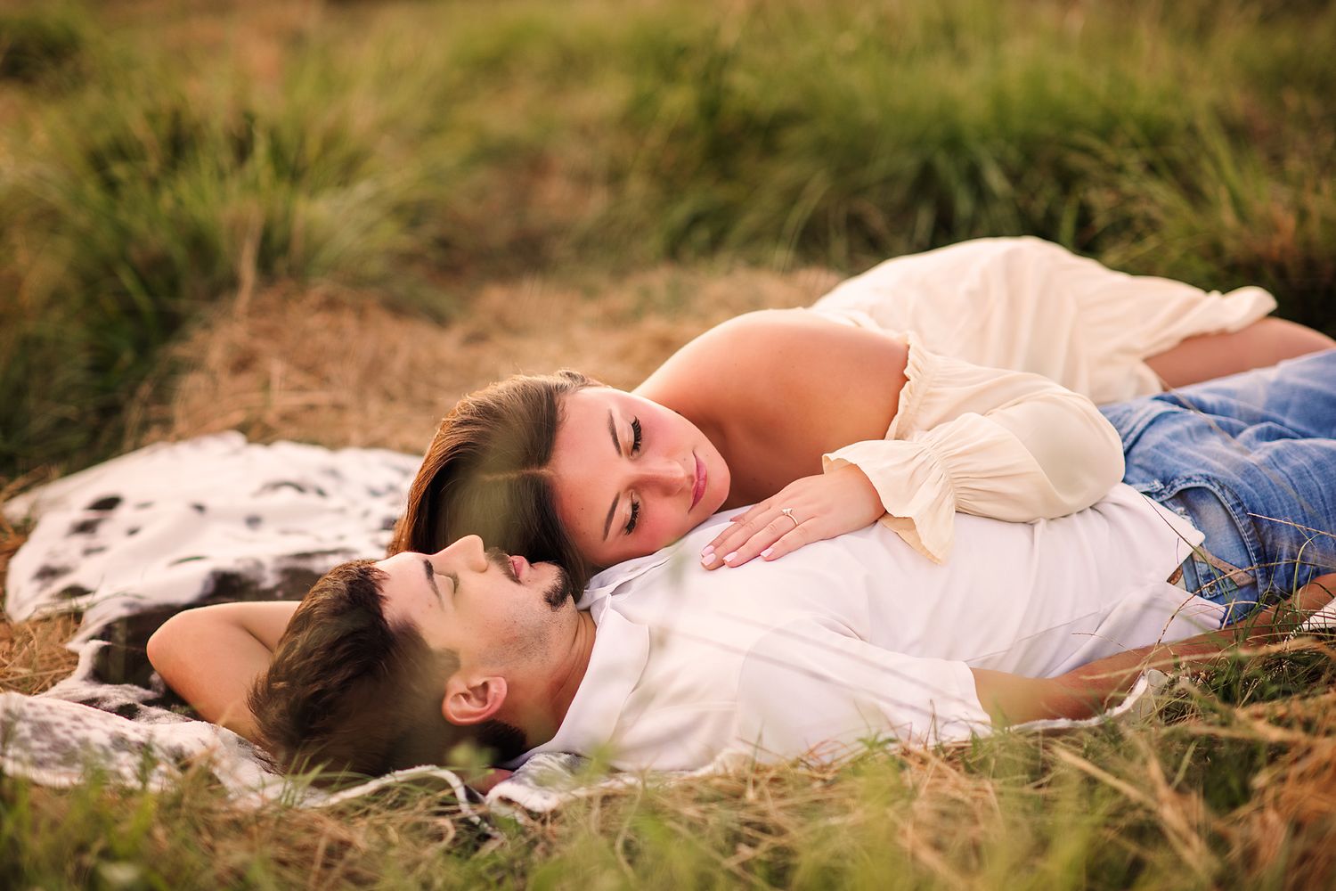 Romantic couple lying together on a blanket in a golden grassy meadow.