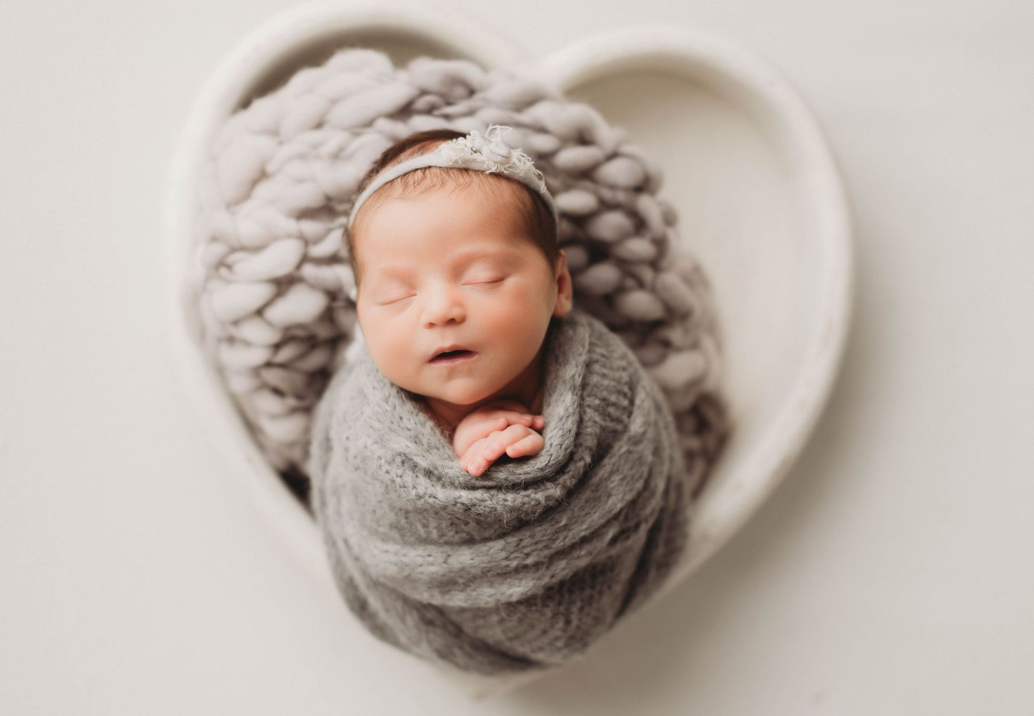 Newborn baby swaddled in white fabric wearing sparkly headband.