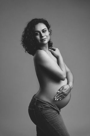 Black and white maternity portrait showing side view of expectant mother in jeans.