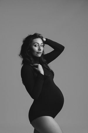 Black and white portrait of a pregnant woman in a black bodysuit posing gracefully in a studio setting.