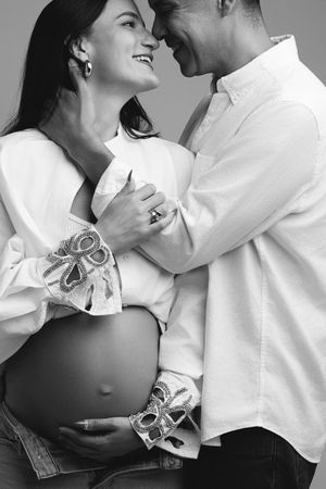 Black and white photo of a smiling pregnant couple in white shirts sharing a tender moment together.