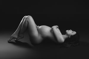 Black and white artistic maternity photo of a pregnant woman reclining gracefully on a studio floor.