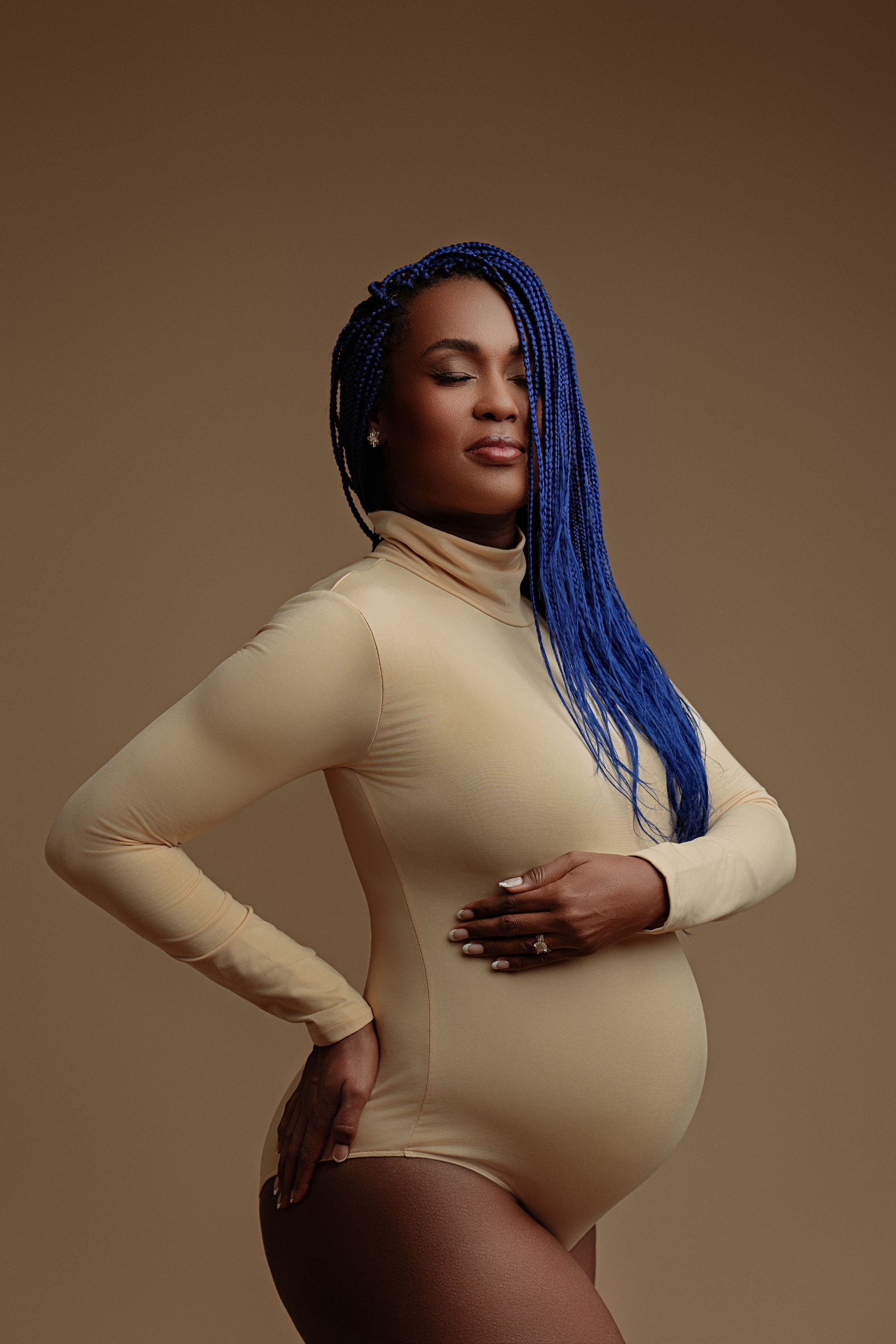 Stylish maternity photo featuring bright blue braids and beige bodysuit against brown background.