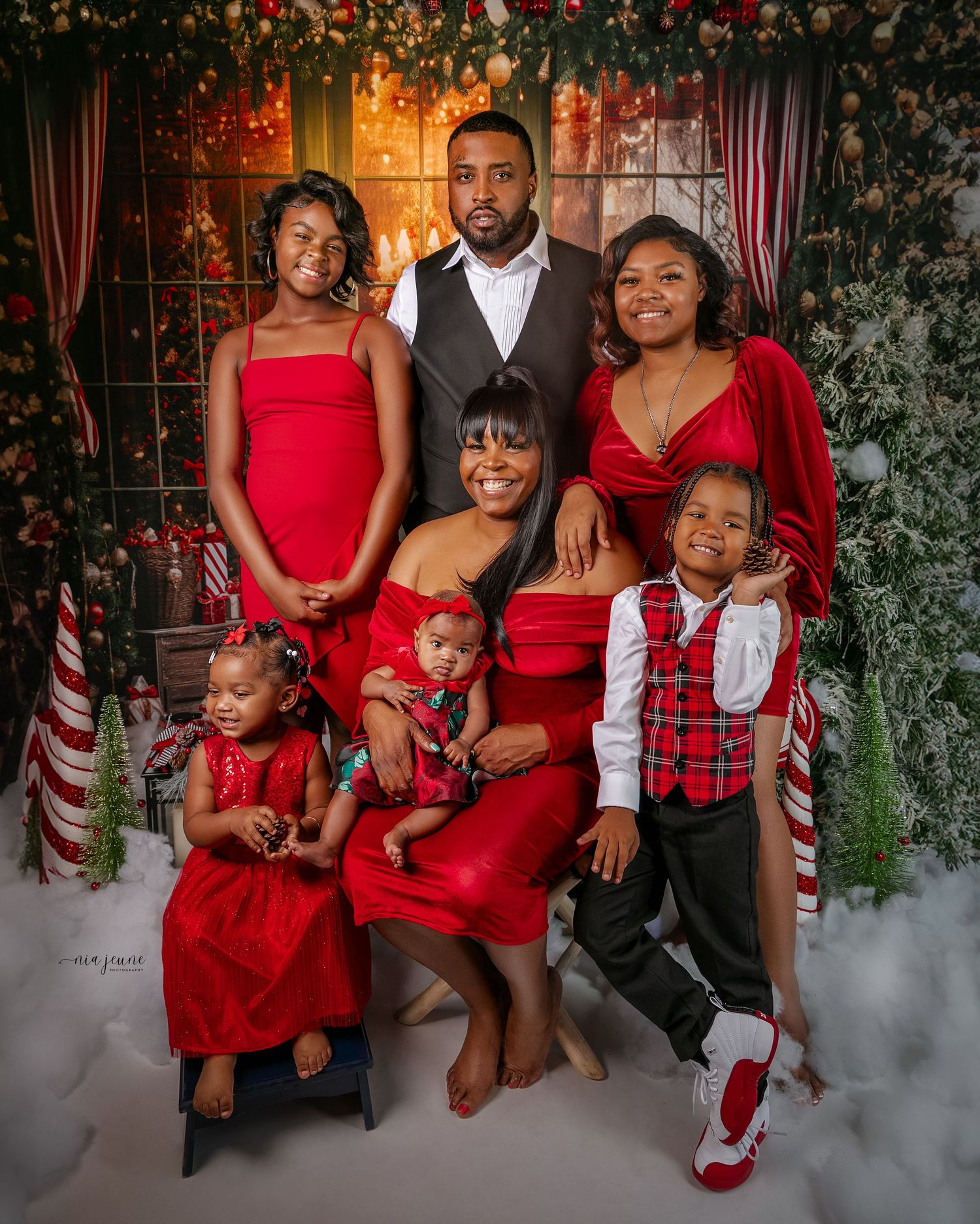 Family holiday portrait with everyone dressed in red outfits against a festive Christmas backdrop.