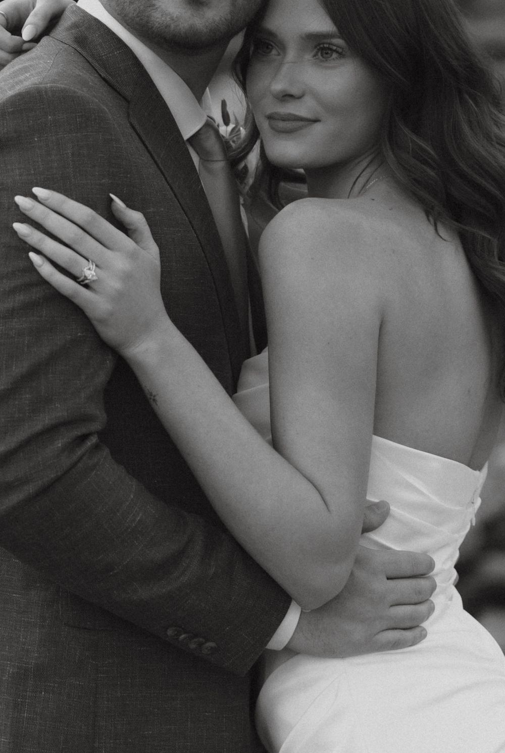 Black and white romantic portrait of bride and groom embracing, showcasing engagement ring.