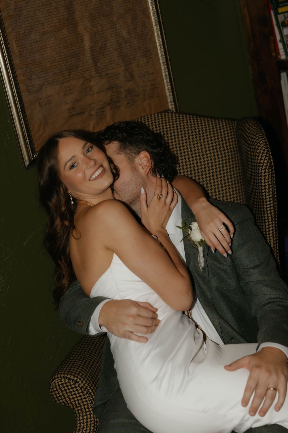 Bride and groom share an intimate moment, with groom kissing bride's cheek as she smiles in white dress.