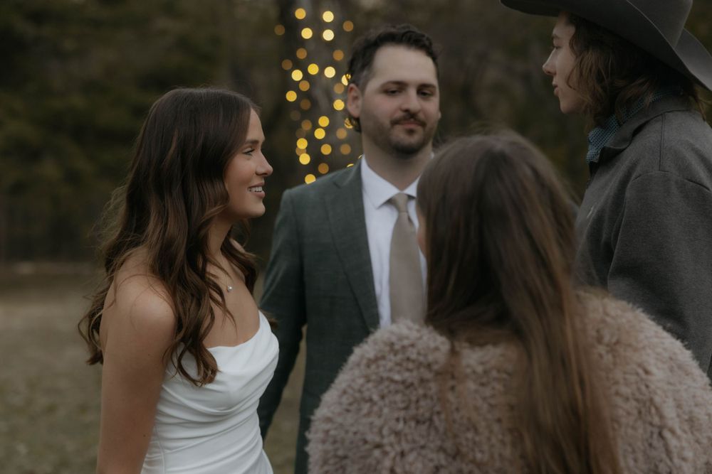 Bride and groom smile warmly while greeting guests at their outdoor autumn wedding celebration.