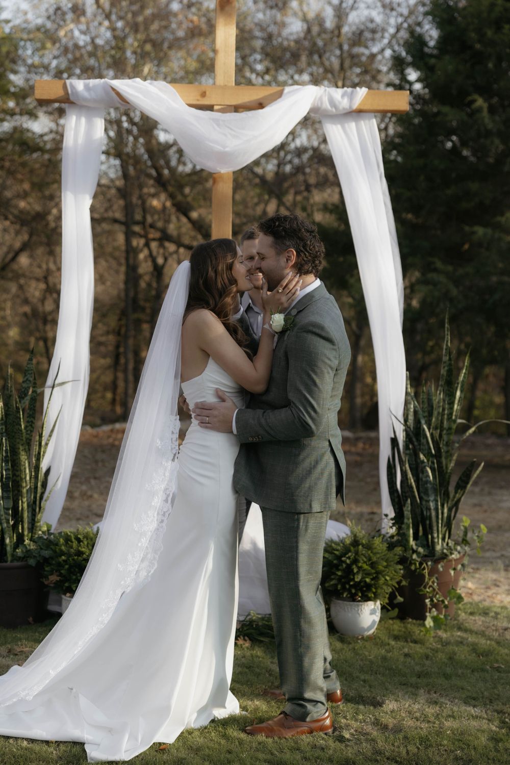 Bride and groom share first kiss under wooden cross wedding arch.