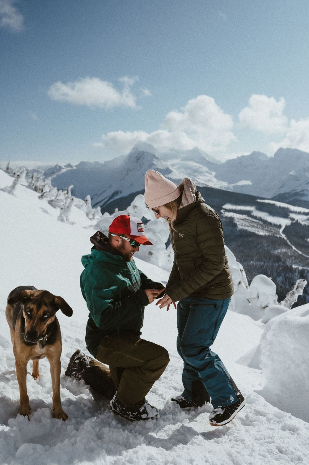 An emotional proposal moment unfolds in the snow with majestic mountain peaks in the background.