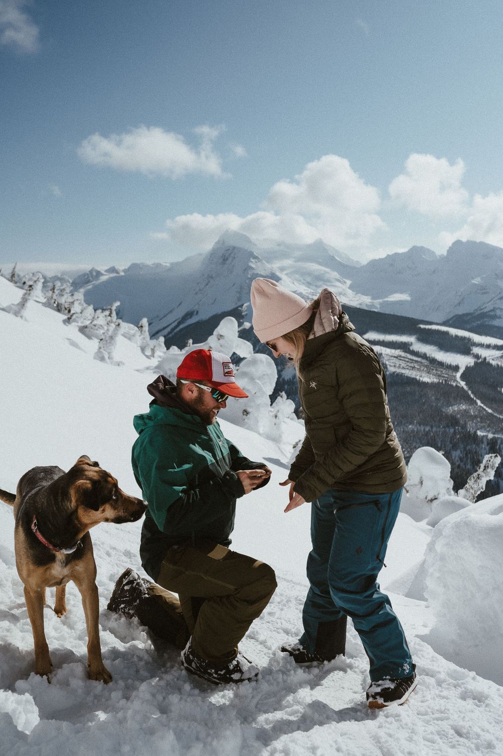A winter mountain proposal scene with a loyal dog watching the special moment unfold.