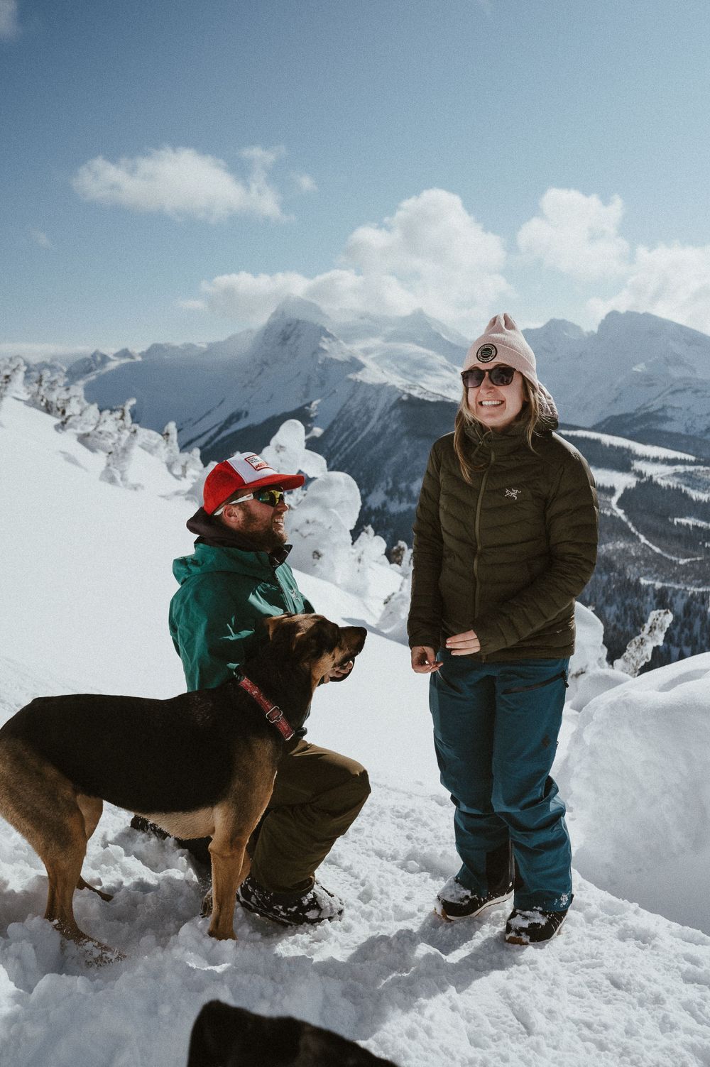 A happy moment captured after a mountain-top proposal with their dog in the snowy landscape.