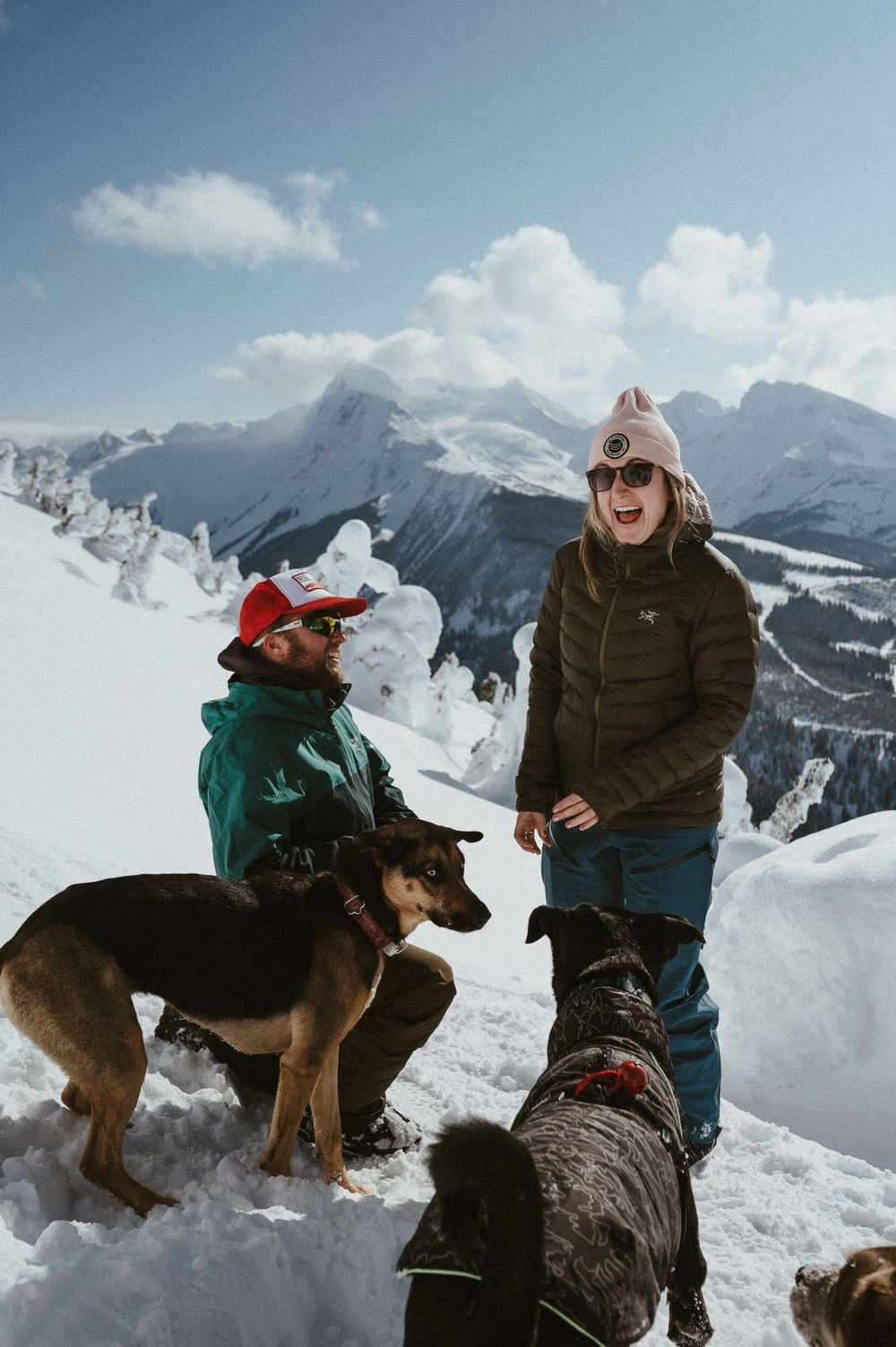 A celebratory moment shared between a newly engaged couple with their dogs in the snowy mountains.