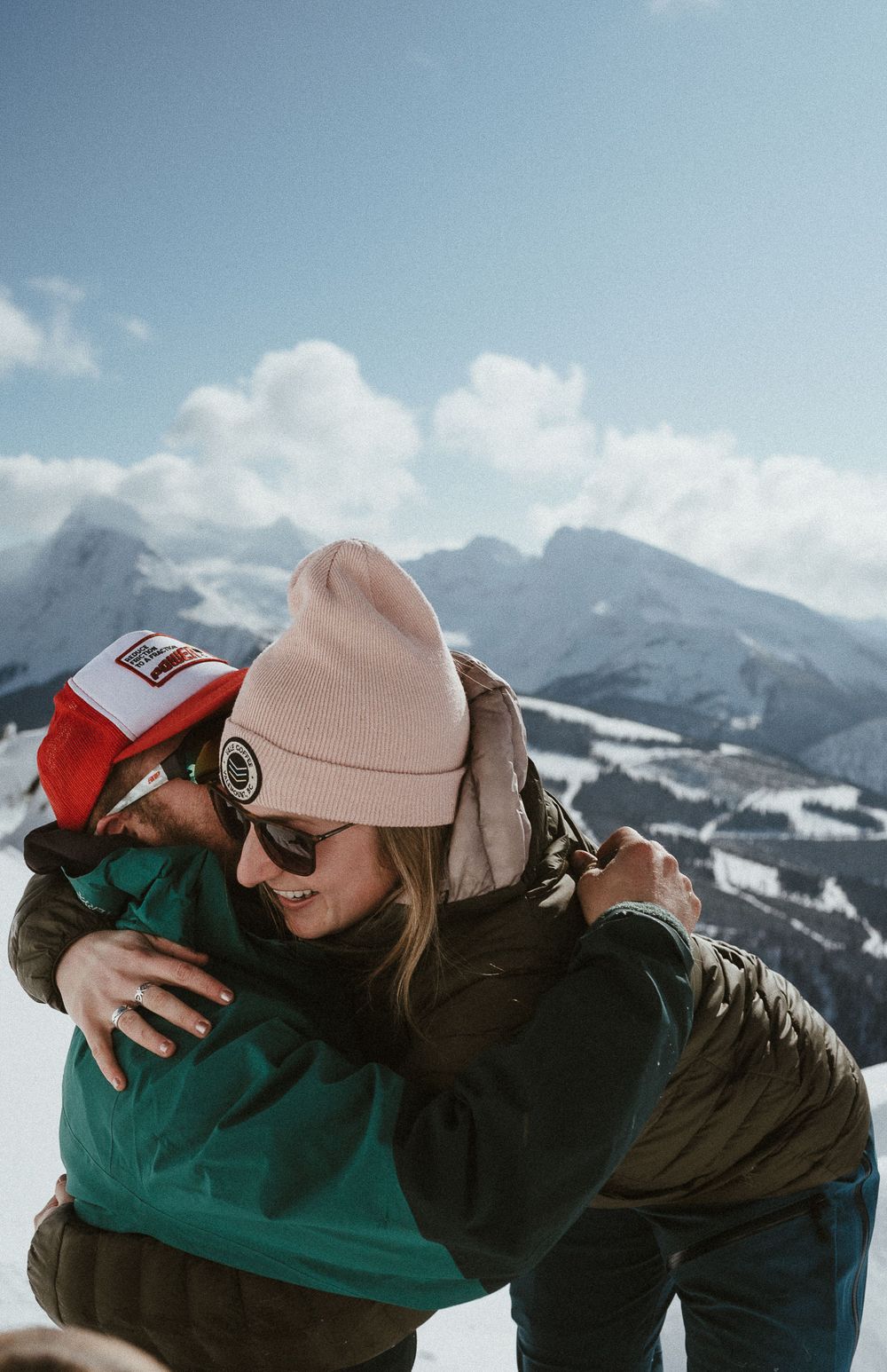 A joyful embrace captured against a backdrop of snow-capped mountains on a clear day.
