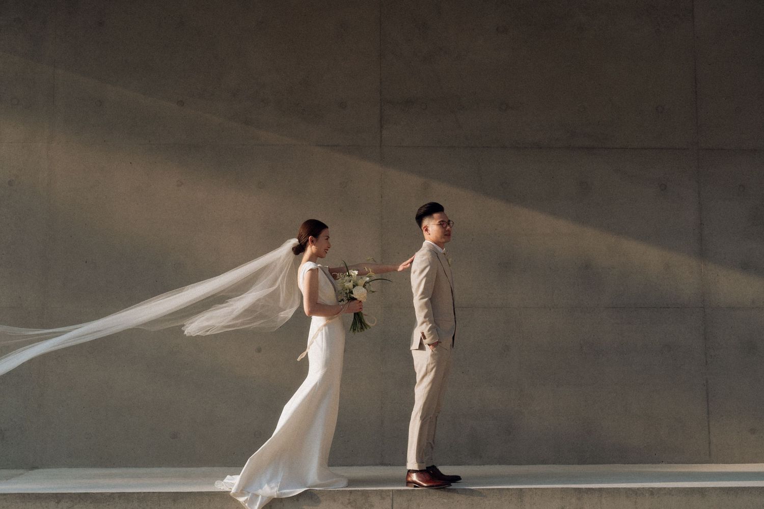 Dramatic wedding photo with flowing veil in minimalist concrete setting.