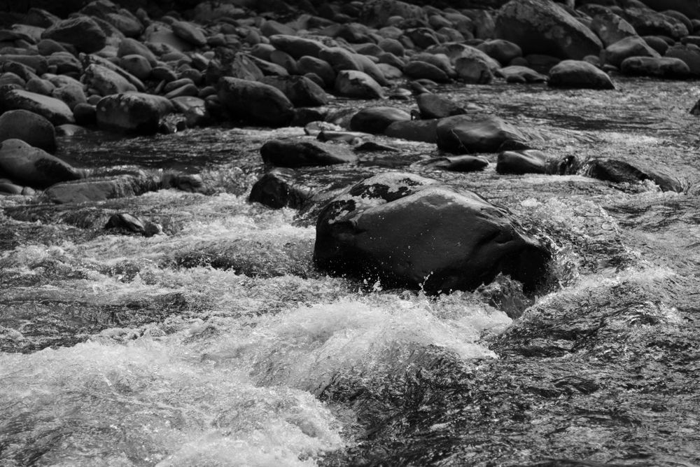 Black and white photo of rushing water flowing over rocks in a mountain stream.