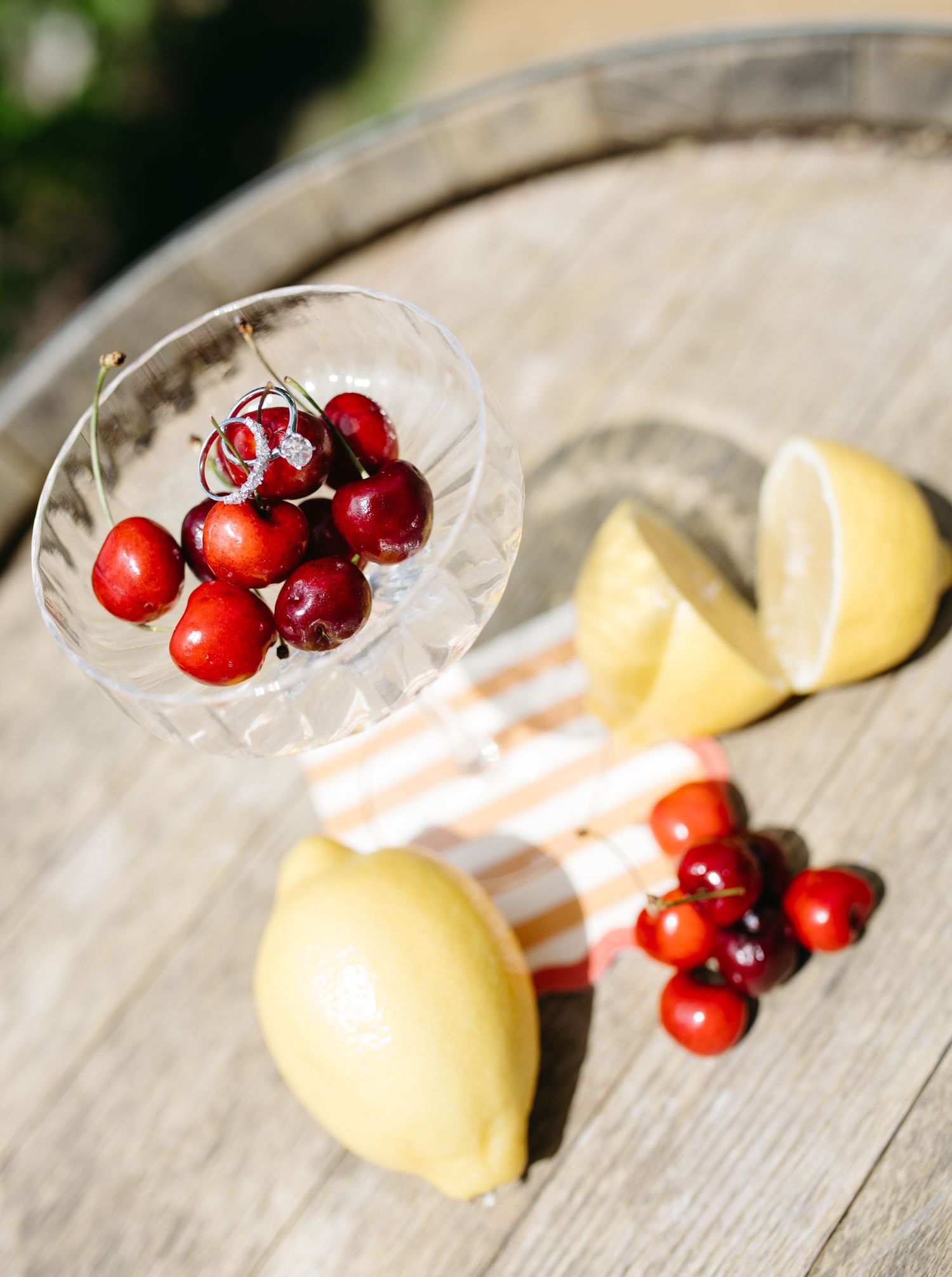 Fresh cherries in a crystal glass with lemon wedges on a rustic wooden barrel surface.