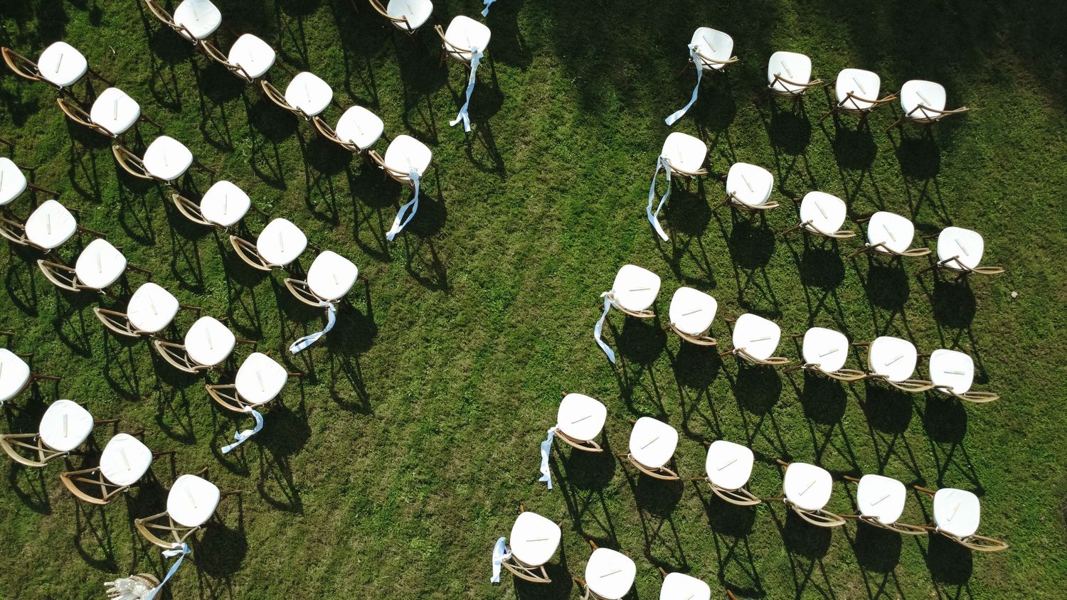 Aerial view of white chairs arranged in rows on green grass for an outdoor ceremony or event.