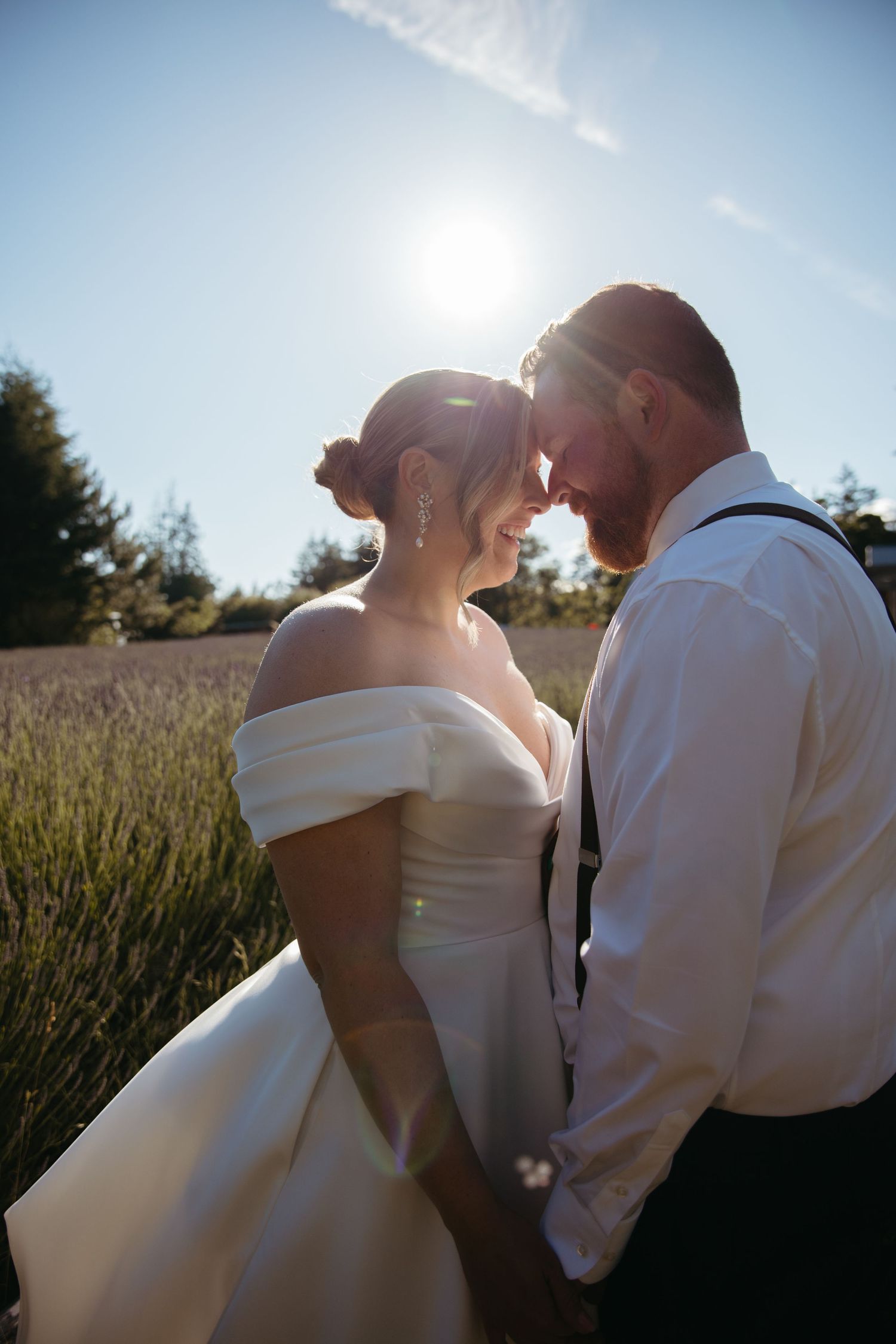 Bride and groom touching foreheads in golden sunlight in a lavender field, bride in off-shoulder white gown.