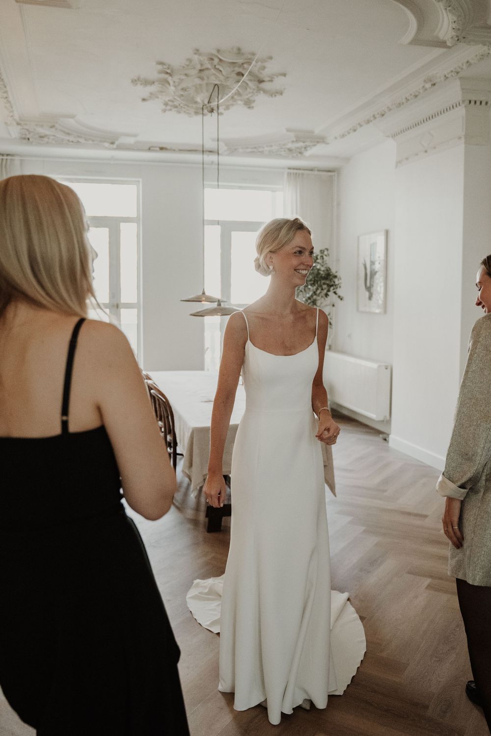 A minimalist white wedding dress in an elegant room with herringbone floors and ornate ceiling details.