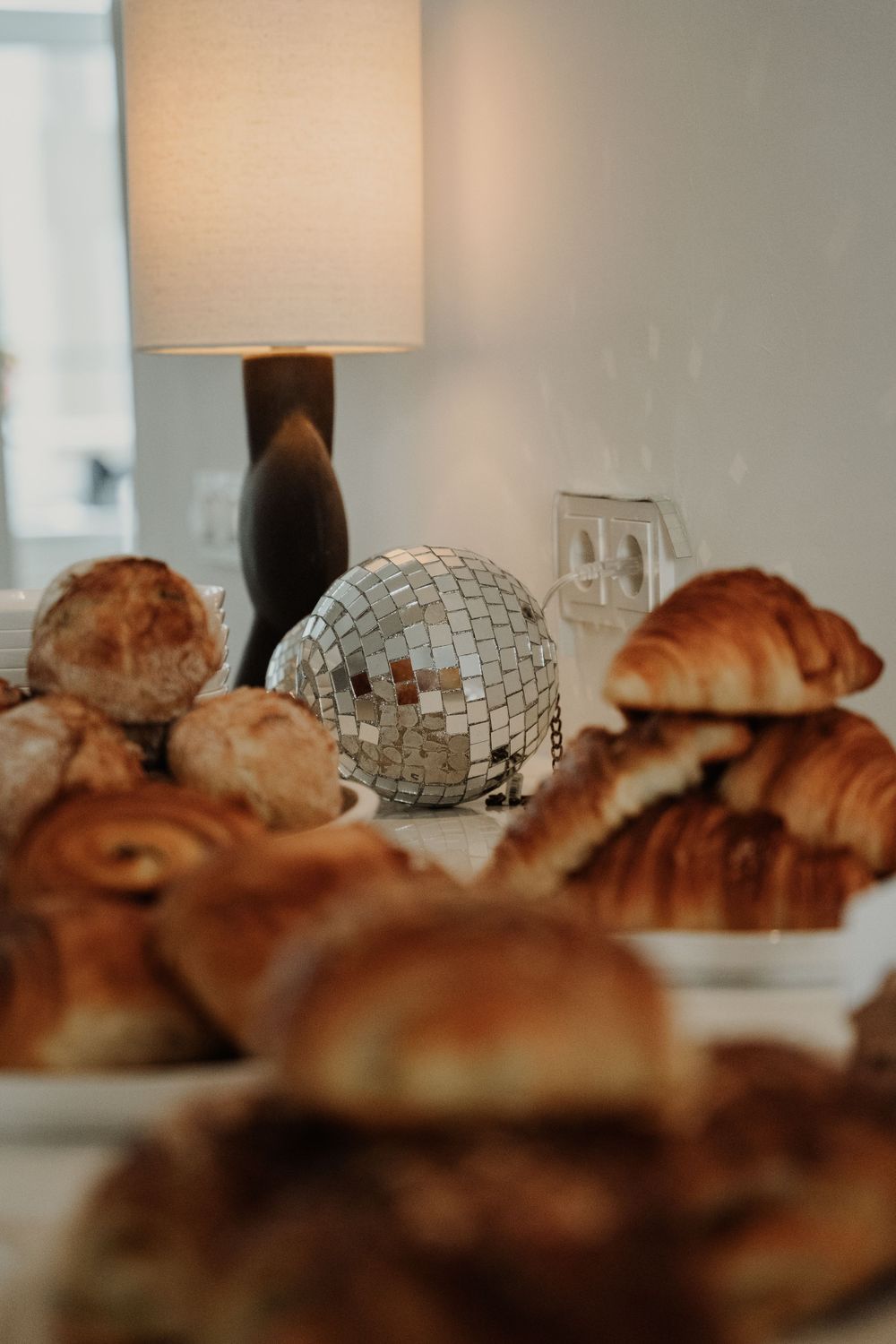 Fresh baked croissants and pastries arranged on a table with a decorative disco ball and table lamp.