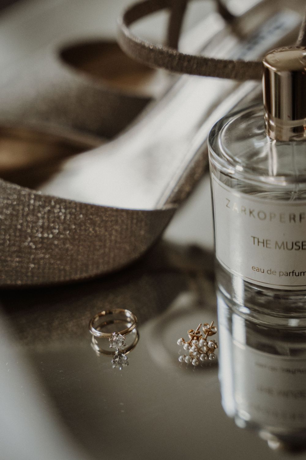 Wedding accessories including a perfume bottle labeled 'The Muse', delicate jewelry, and elegant shoes in neutral tones.