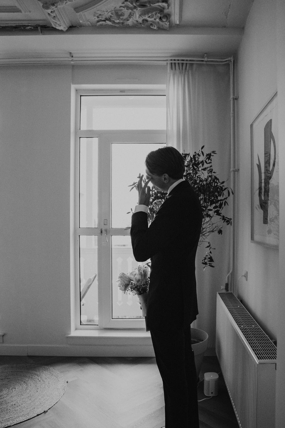 A black and white photo of a silhouetted figure standing by a window in a minimalist interior space.