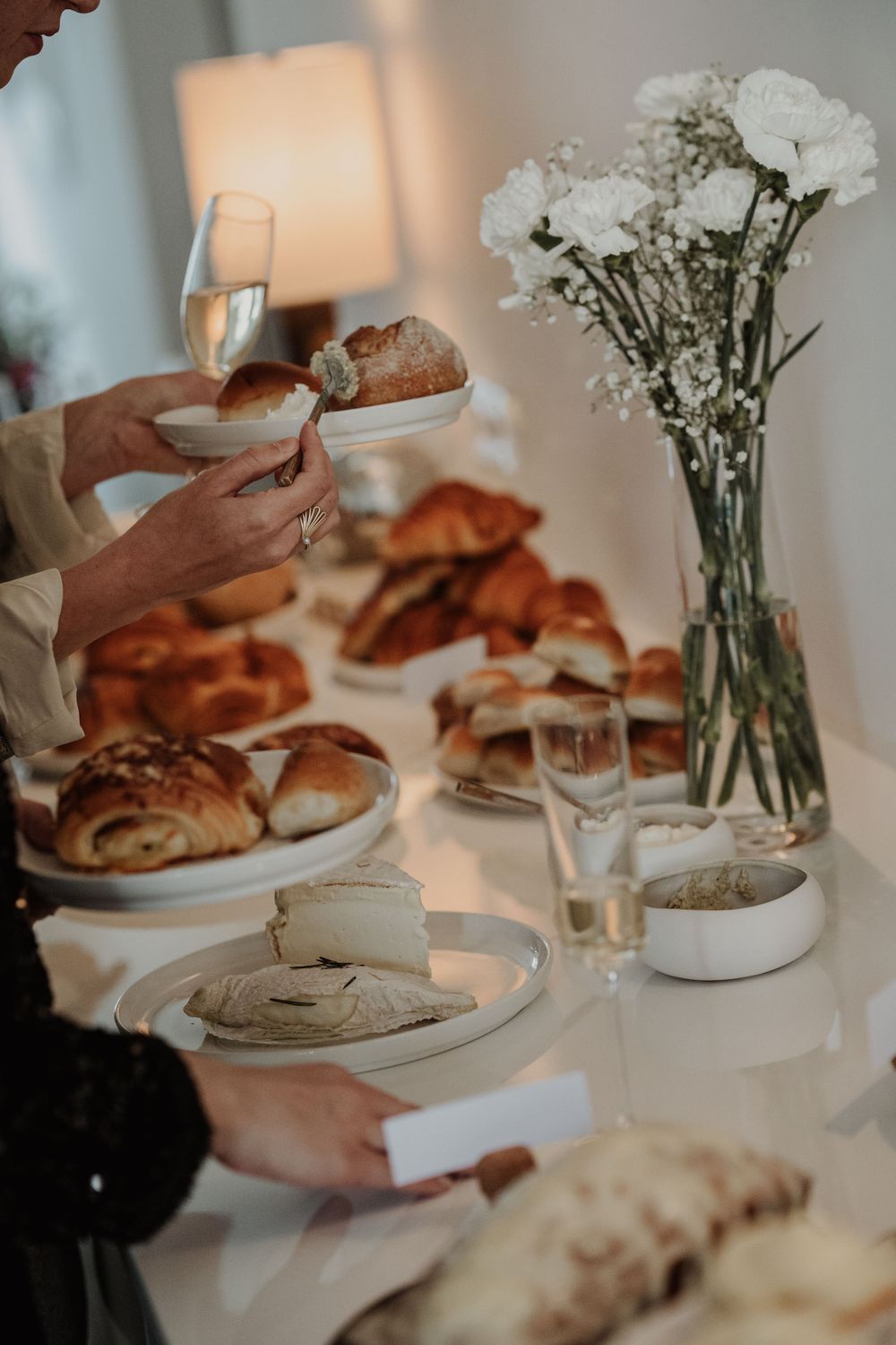 Elegant table setting with fresh pastries, champagne glasses and white carnations in a vase creating a cozy brunch atmosphere.