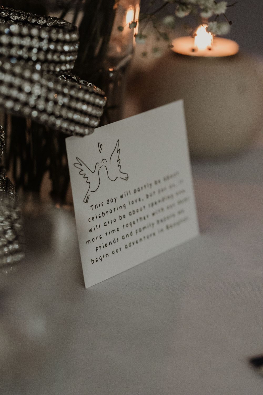 A white card with a dove illustration sits beside a glowing candle in a moody, atmospheric setting.
