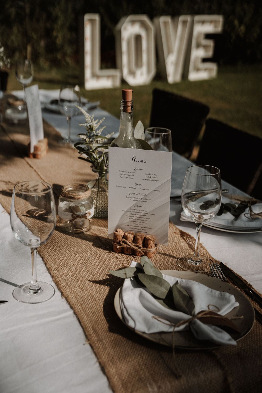 An elegant wedding table setting with illuminated LOVE sign, menu card, and rustic decor elements.