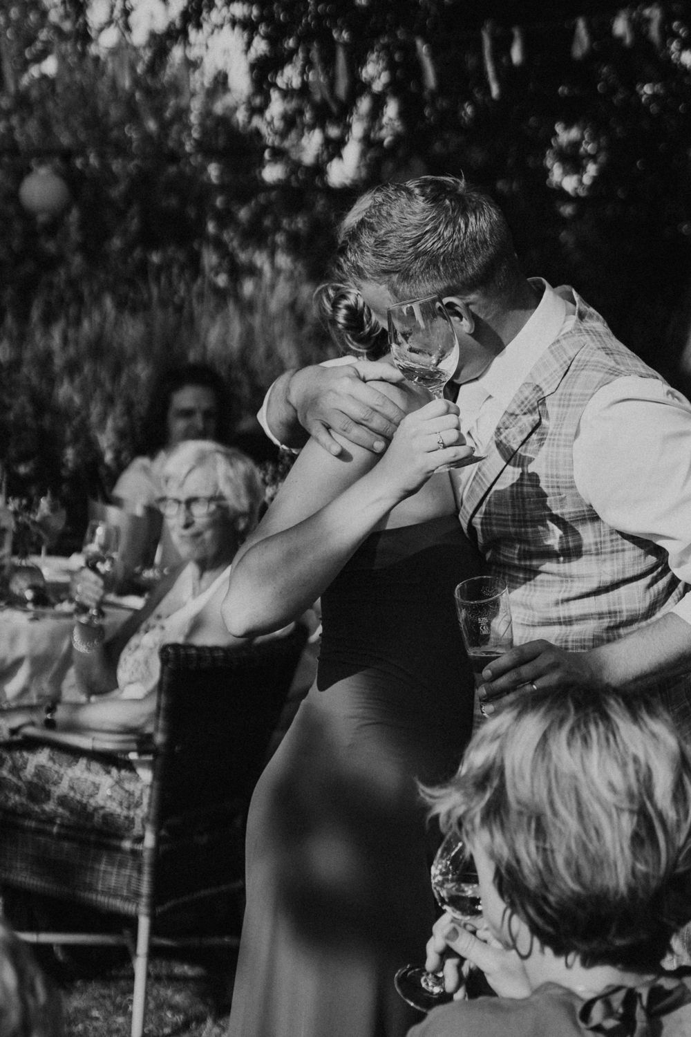 A vintage black and white photo of guests enjoying drinks and laughter at an outdoor garden party.