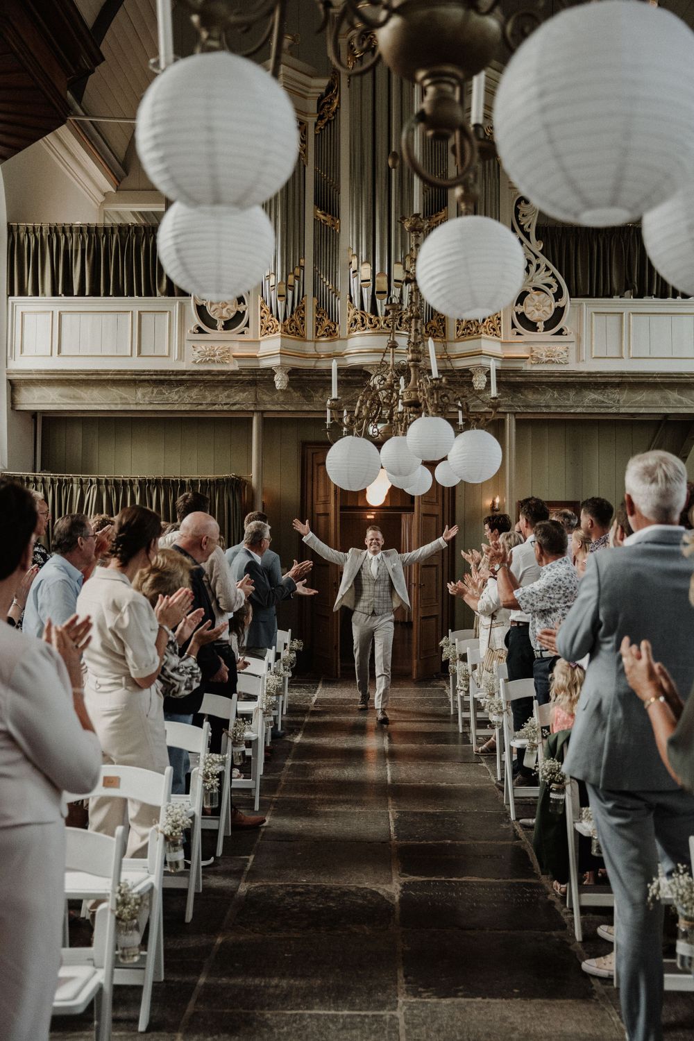 Wedding ceremony in an elegant hall decorated with white paper lanterns and rows of white chairs.