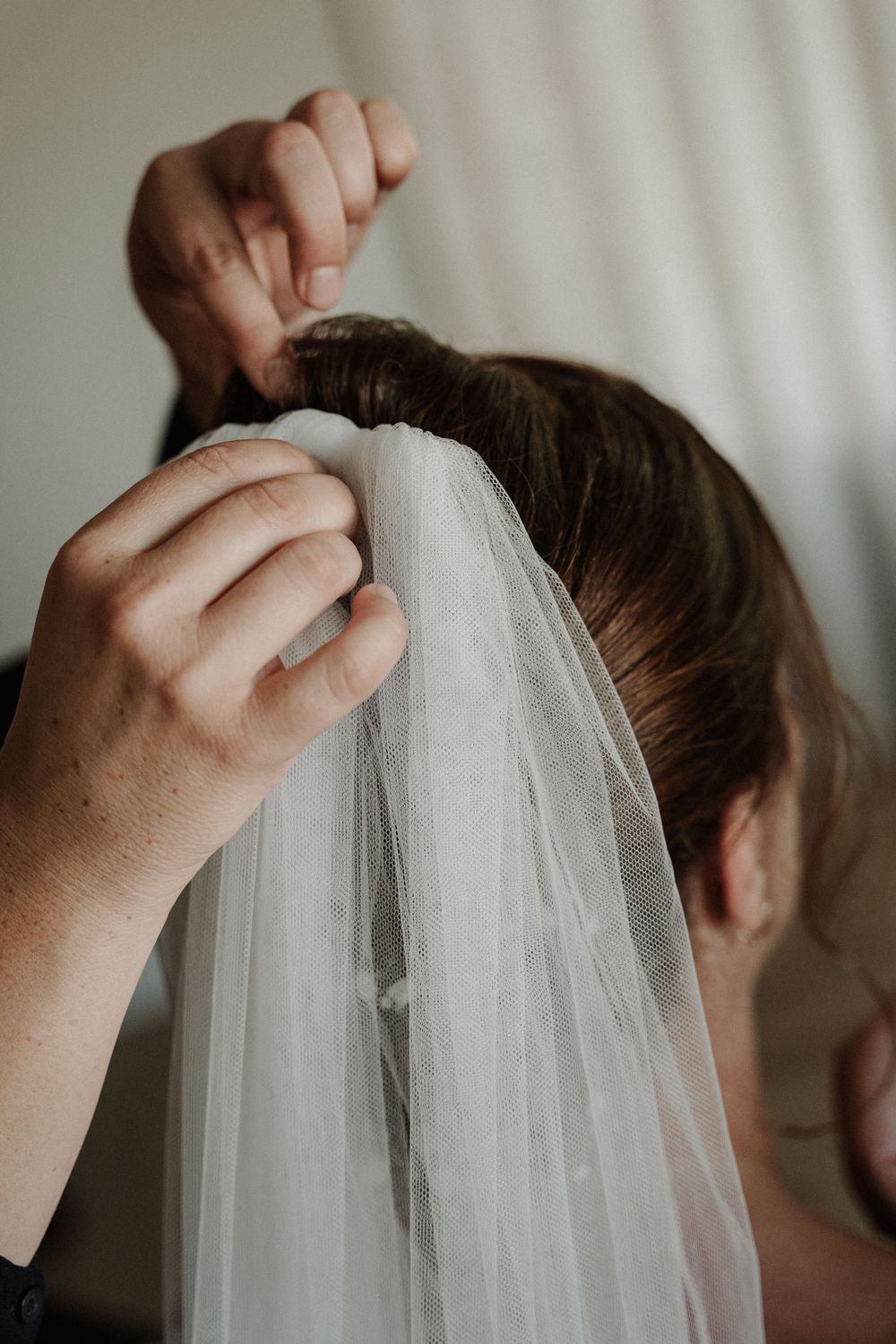Hands carefully adjusting a delicate white bridal veil during wedding preparations.