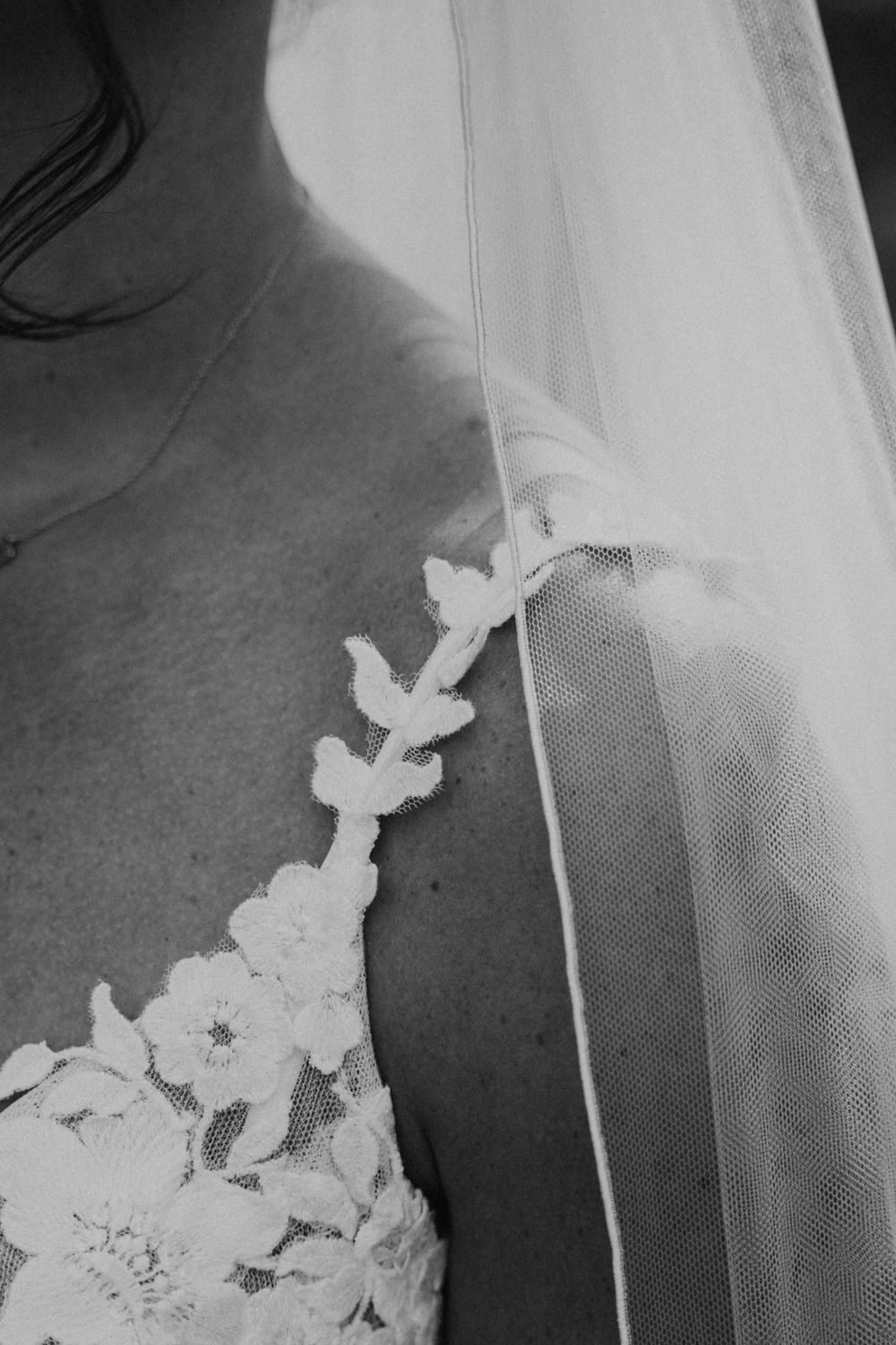 Close-up black and white detail of delicate lace applique and tulle veil on a wedding dress.