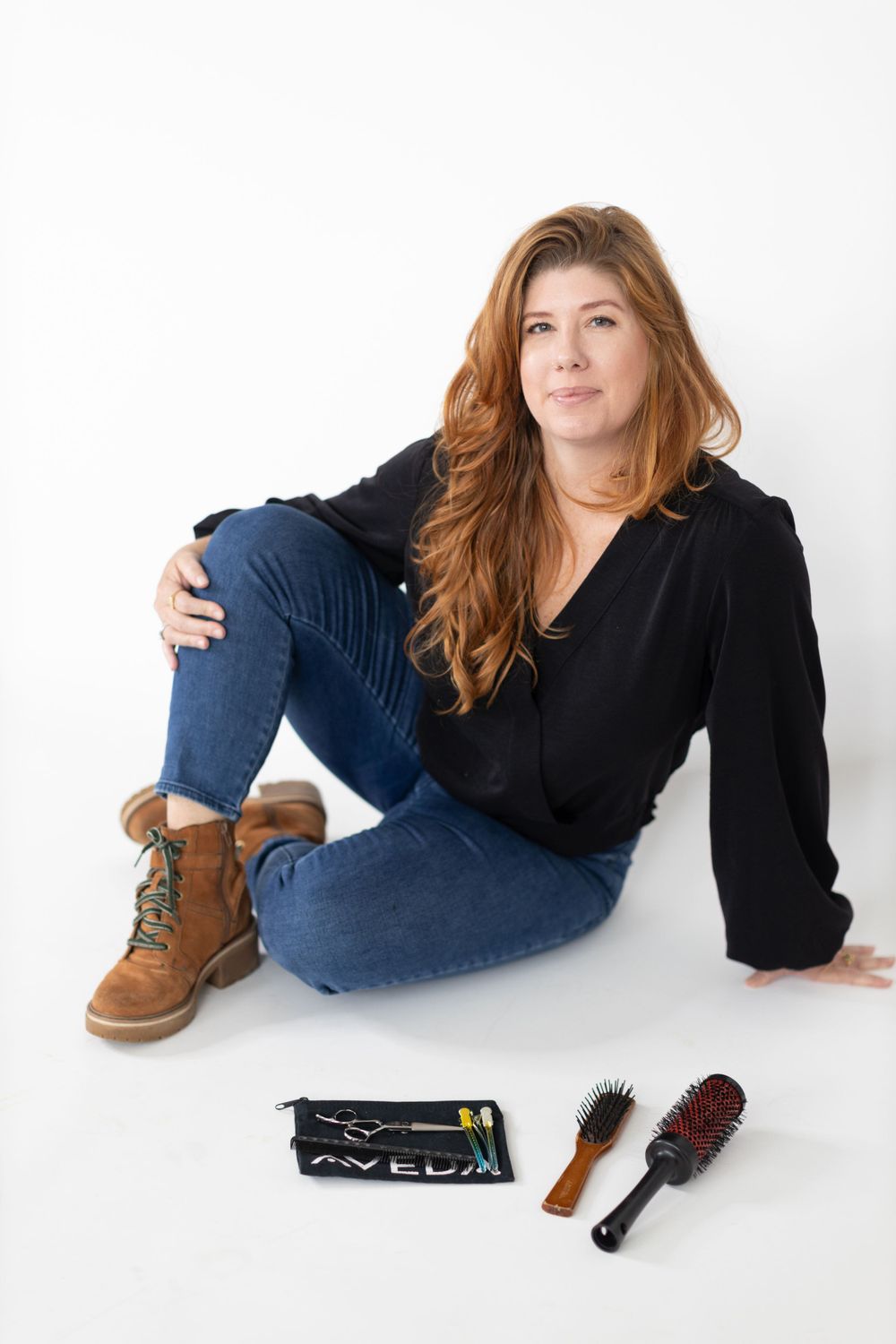 Casual lifestyle portrait with brown boots, jeans, black sweater, and hair styling tools arranged on white background.