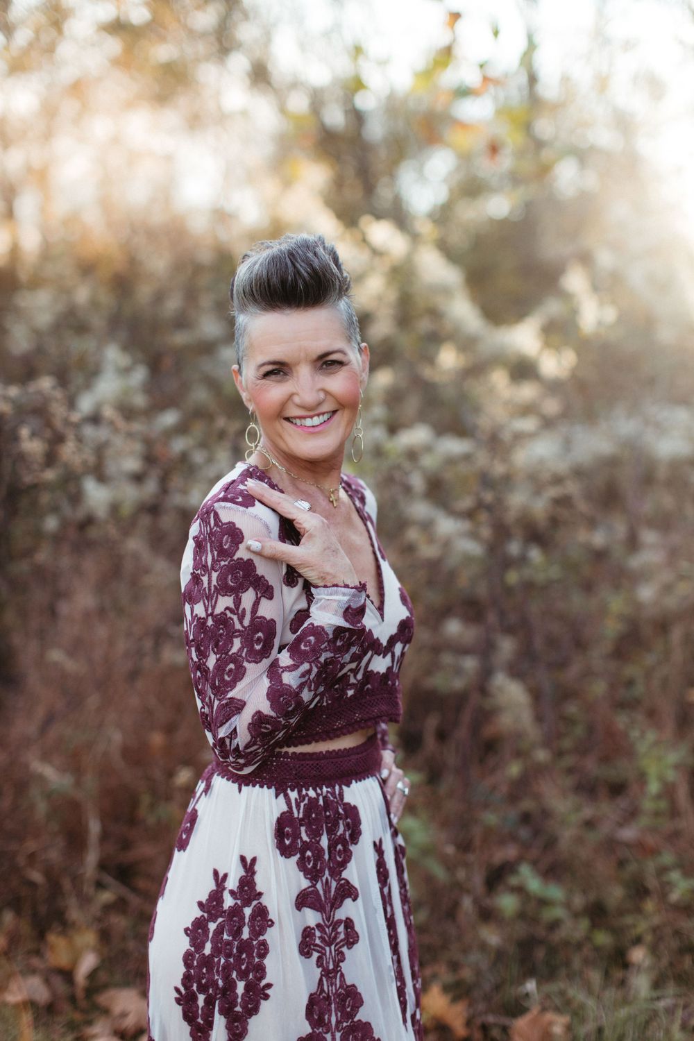Woman in burgundy and white floral dress poses outdoors with a fashionable updo hairstyle.